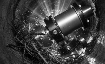 A robotic pipe inspection device equipped with cameras and lights moves through a pipe, illuminating water droplets and tangled tree roots inside.
